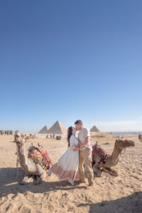 Kamy and Eric kissing between two camels, with the Pyramids of Giza in the background.