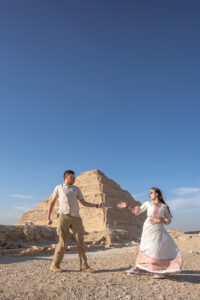 Kamy and Eric playing Rock, Paper, Scissors while posing like the people in ancient Egypt drawings, in front of the Step Pyramid of Djoser