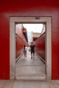 Kamy and Eric holding hands walking in a Chinese style corridor in red colour.