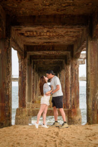 Kamy and Eric kissing under a bridge on a beach.