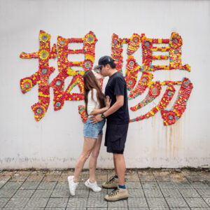 Kamy and Eric kissing in front of a wall with Chinese words "Jieyang"