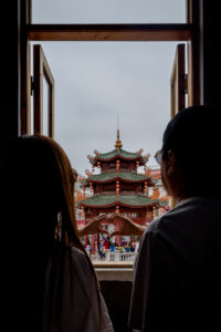 Kamy and Eric creating a heart hand sign together in front of a Chinese style Pavilion.