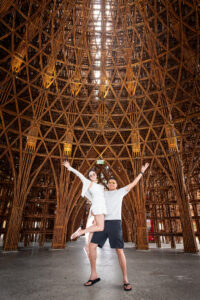 Eric lifting Kamy with one arm, under a bamboo structure.