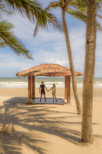 Kamy and Eric holding hands under a beach hut.